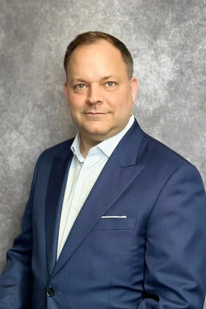 Formal business portrait of a man in a blue suit against a gray background.
