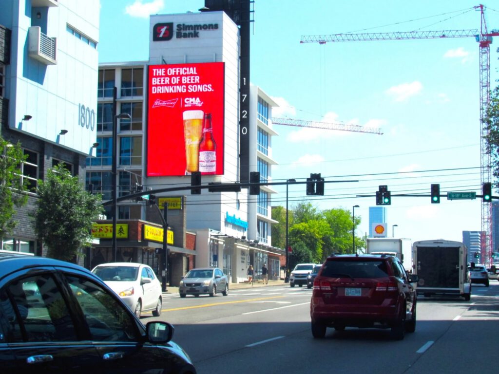 City street with cars, buildings, and digital billboard advertising beer.