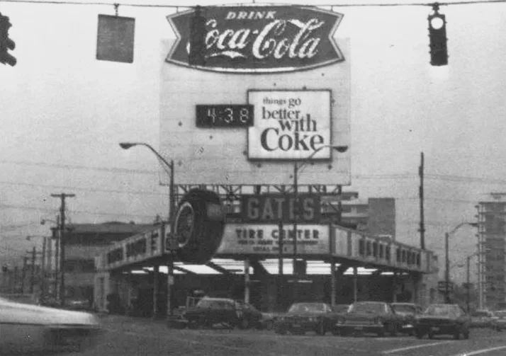 Black and white photo of a vintage Coca-Cola billboard and gas station.